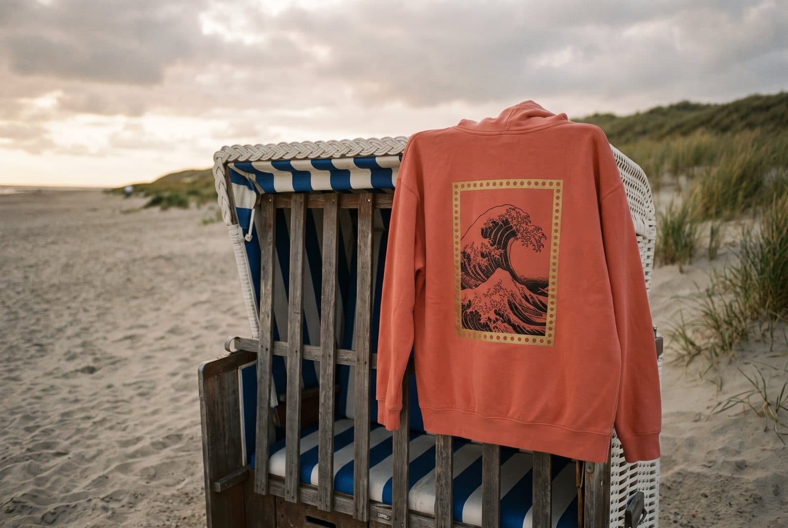 Korallenfarbener Hoodie „Die Welle“ über einem Strandkorb